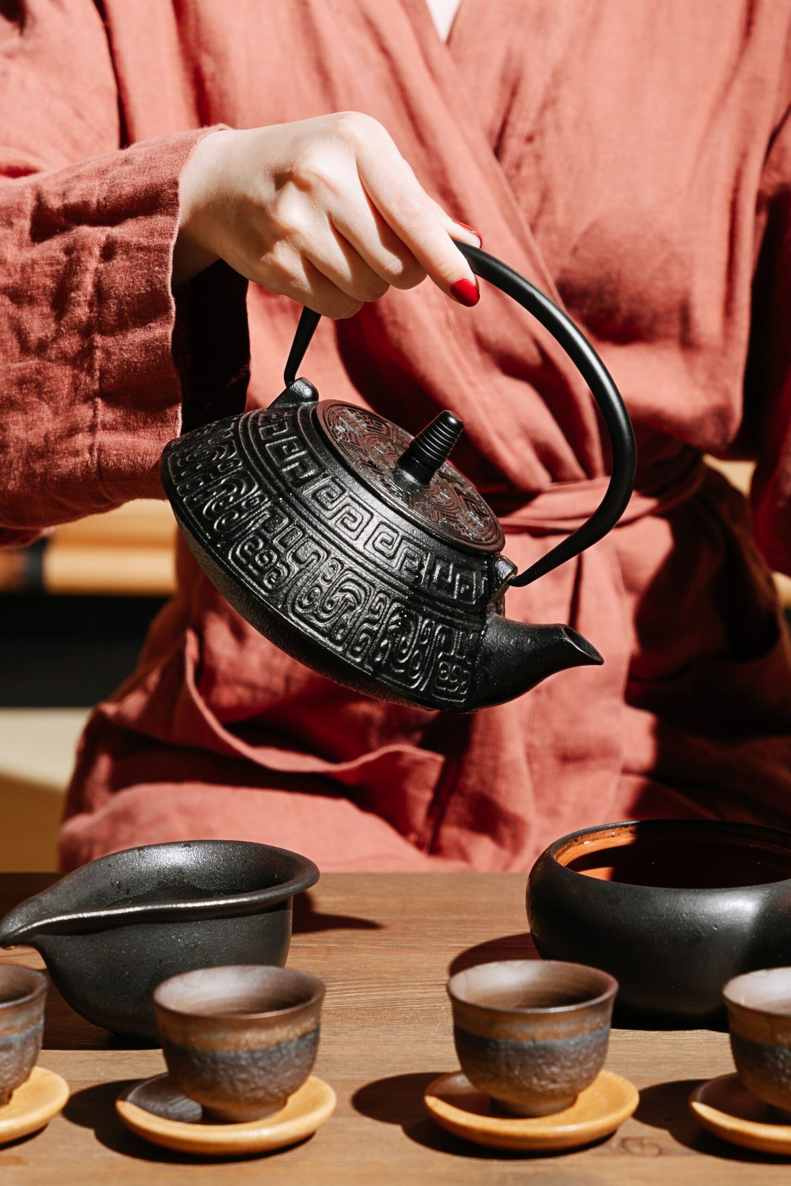 Close-up of a woman pouring tea from a Chinese teapot in a zen-like setting.